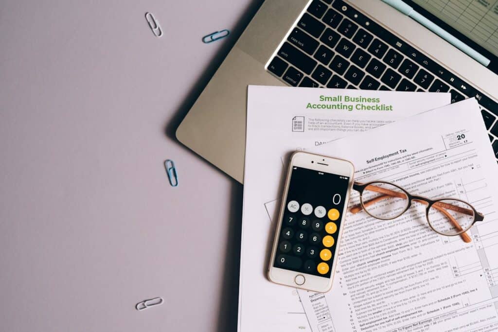 pexels-photo-8962451 Flat lay of small business accounting tools including tax form, phone, and glasses on a desk.